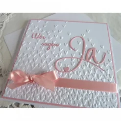 Einladungskarte zur Hochzeit in weiß/rosa, mit geprägtem Hintergrund, und *Wir sagen Ja* Schriftzug