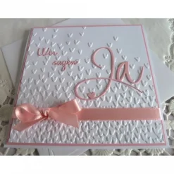 Einladungskarte zur Hochzeit in weiß/rosa, mit geprägtem Hintergrund, und *Wir sagen Ja* Schriftzug