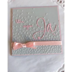 Einladungskarte zur Hochzeit in grau/rosa, mit geprägtem Hintergrund, und "wir sagen Ja" Schriftzug