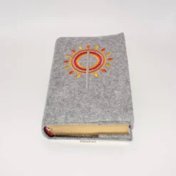 Gotteslobhülle, Filz, grau, bestickt mit grauem Kreuz, mit orangen, gelben Strahlen, die wie eine Blume angeordnet sind