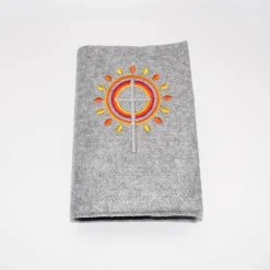 Gotteslobhülle, Filz, grau, bestickt mit grauem Kreuz, mit orangen, gelben Strahlen, die wie eine Blume angeordnet sind
