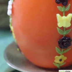 große Ostereikerze in orange mit doppelter, frühlingshafter Blumenranke verziert, Osterdeko, Ostergeschenk